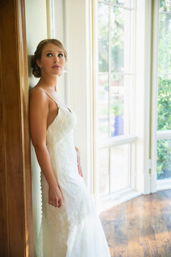Portrait of young bride in home leaning on doorframe looking up towards the second floor 