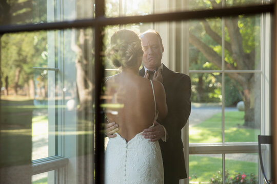 Bride fixing her fathers bow tie, seen through window