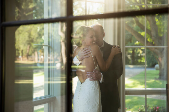 Bride and father of the bride embracing celebrating the wedding day, seen through window