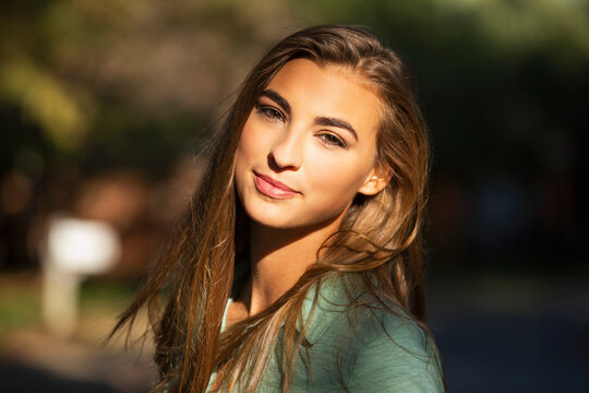 Portrait of young woman standing outside in bright sun, looking into camera lens 