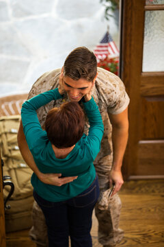 Mother welcomes her soldier son home after deployment , embracing in doorway