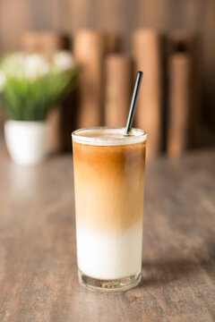 Close up of a cup of latte with background of wood and plant.