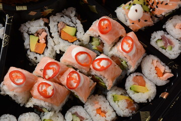 Set of sushi rolls  on a black plastic platter decorated with soy sauce and spices. Ready for delivery