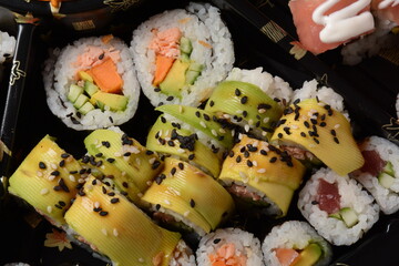 Set of sushi rolls  on a black plastic platter decorated with soy sauce and spices. Ready for delivery