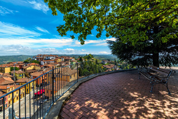 Bench under trees and view on small town in Piedmont, Italy.