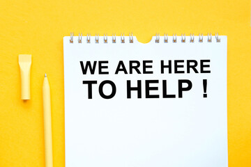 Notebook, pen and words WE ARE HERE TO HELP. on yellow background.