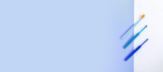 Dental care conept. Dentistry tools. Three blue toothbrushes for braces on white and blue background. still life, flat lay. Extra wide banner with copyspace.