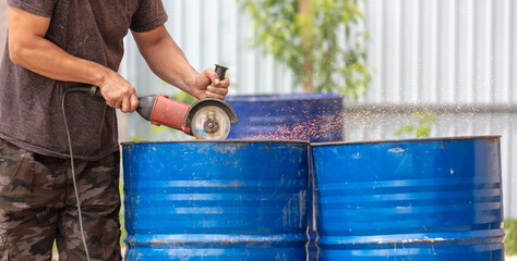 A worker cuts metal barrels.