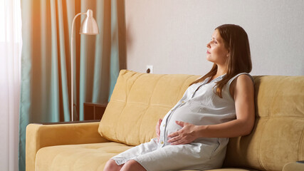 Young pregnant woman stroking belly while sitting on the sofa.