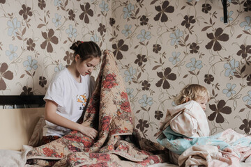 Children helping with cleaning the house, removing bed linen, doing chores. Lifestyle, brother and sister, family.