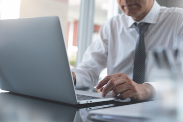 Businessman working on laptop computer with business document on table in modern office