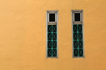 Glass windows with ventilation and wrought iron to prevent thieves on the walls of an old building painted in classic yellow.