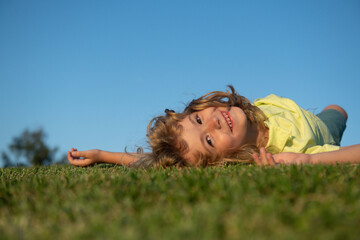 Kid playing in the meadow. Happy healthy caucasian child boy with lying on the grass field background. Little child in beautiful green environment. Amazing happy kids outdoor.