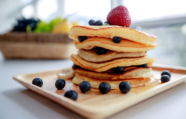 in kitchen on bright morning, pancake tower on wooden plate topping by strawberry and blueberry look very sweet tasty prepared to be served as superb healthy dessert after breakfast