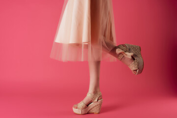 female legs in beige shoes posing close-up pink background