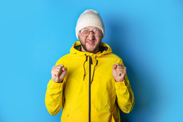 Bearded young man closing his eyes squinting fists clenched on a blue background