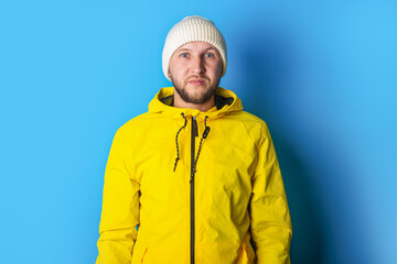 Serious bearded young man in a yellow jacket on a blue background