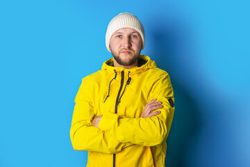 Bearded young man in a yellow jacket with crossed arms on a blue background