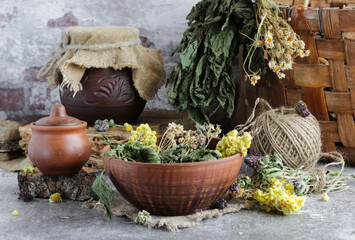 Obraz na płótnie Canvas Ceramic bowl with medicinal dried herbs of chamomil,tansy,clover,nettle on the background rustic wicker basket.