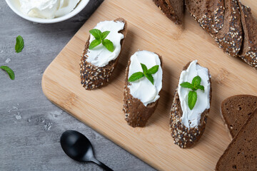 Home made bread on a wooden cutting board with curd cheese and ricotta and herbs. Decorated with...