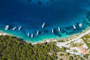 Top down aerial view of sailing boats docked in blue bay of Fiskardo, Kefalonia island, Ionian, Greece