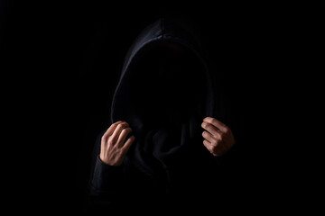 A woman's face is not visible in a black robe holding the hood with her palms on a black background