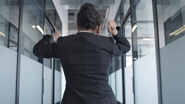 Back view of excited business woman dancing in office, happy with promotion