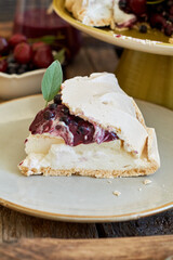 Pavlova cake with blueberry curd, cherries, blueberries and sage. Side view. Wooden background.