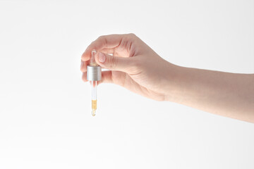 female hand holding a dropper with oil, essence, cosmetic product isolated on white background,...