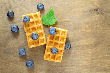 Fototapeta na wymiar Soft Belgian waffles with blueberries on the background of a brown wooden table with a natural pattern, top view, copy space