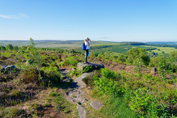 Fototapeta na wymiar Young girl standing on a rock on Birchen Edge in the Derbyshire countryside taking pictures of the landscape