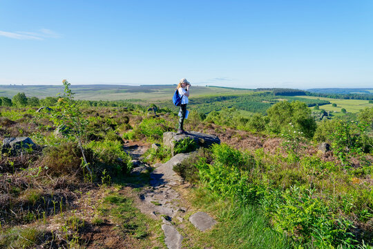 Young girl standing on a rock on Birchen Edge in the Derbyshire countryside taking pictures of the landscape