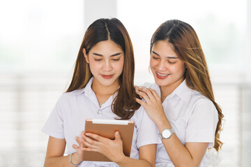 Asian sibling college students in student uniform interacting and looking at a digital tablet to study together on the university campus. Education stock photo