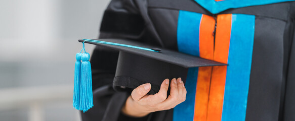 Close-up shot of a university graduate in graduation gown holding a degree certification with...