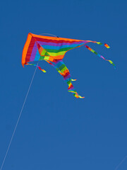 Isolated funny rainbow color kite flying in the blue sky