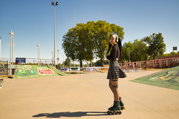 Cute young girl with heterochromia and punk style with white headphones and inline skates holding...