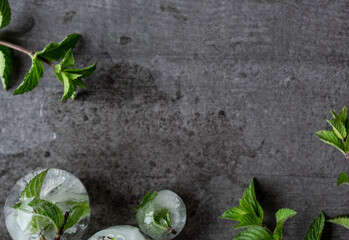 Ice with mint. On a dark modern background with copy space. Round ice cubes with green fresh mint leaves.