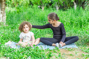 Naklejka na ściany i meble pretty girl teaching yoga to her sister, little girls doing yoga exercises in the garden