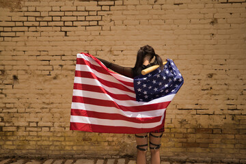 Pretty young girl with pigtails and punk style with a baseball bat behind her neck and a U.S. flag...