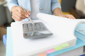 Woman leafing through folder with documents and looking at calculator closeup