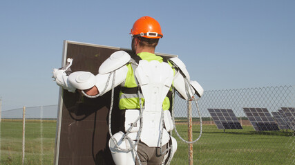 Male technician in exoskeleton carrying photovoltaic panel - obrazy, fototapety, plakaty