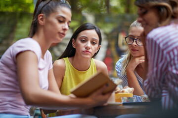 A group of female students is reading a book while they have a drink in the bar. Leisure, bar,...