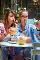 Two young and beautiful female friends making funny grimaces while taking a selfie in the bar. Leisure, bar, friendship, outdoor