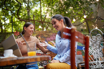 Two cheerful female friends having fun at a bar while watching a laptop content. Leisure, bar, friendship, outdoor