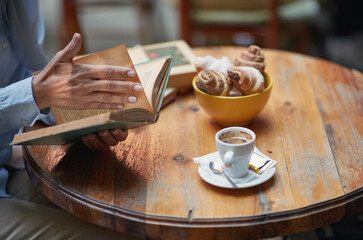 A person reading a book in the bar while enjoying a coffee and croissants. Leisure, bar, outdoor