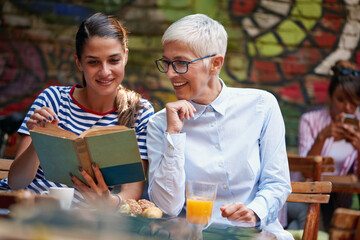 young adult woman reading a book together with elderly caucasian female.