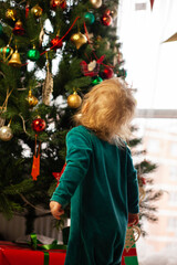 cute little kid looks at Christmas tree decorated with toys and garland. New year and Christmas. Winter holidays. Home comfort. Winter holidays lifestyle. Happy childhood.