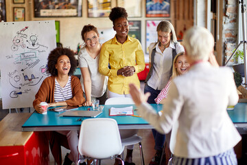 A group of young creative female colleagues in the office is enjoying a meeting with their elderly female boss