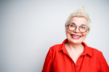 Happy elderly woman in red shirt and glasses smiling broadly and looking at the camera