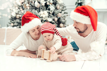 Happy family under Christmas tree. baby boy in Santa Claus hat with gifts under Christmas tree with many gift boxes presents